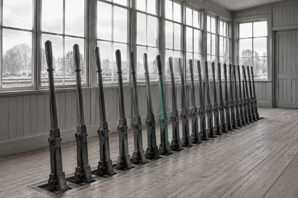 A row of signal levers in an empty signal box; one lever is painted teal.