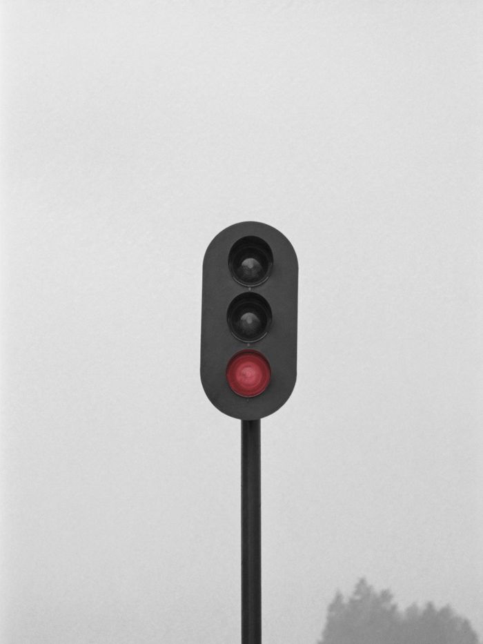 A railway signal against a pale sky, its red lamp lit.