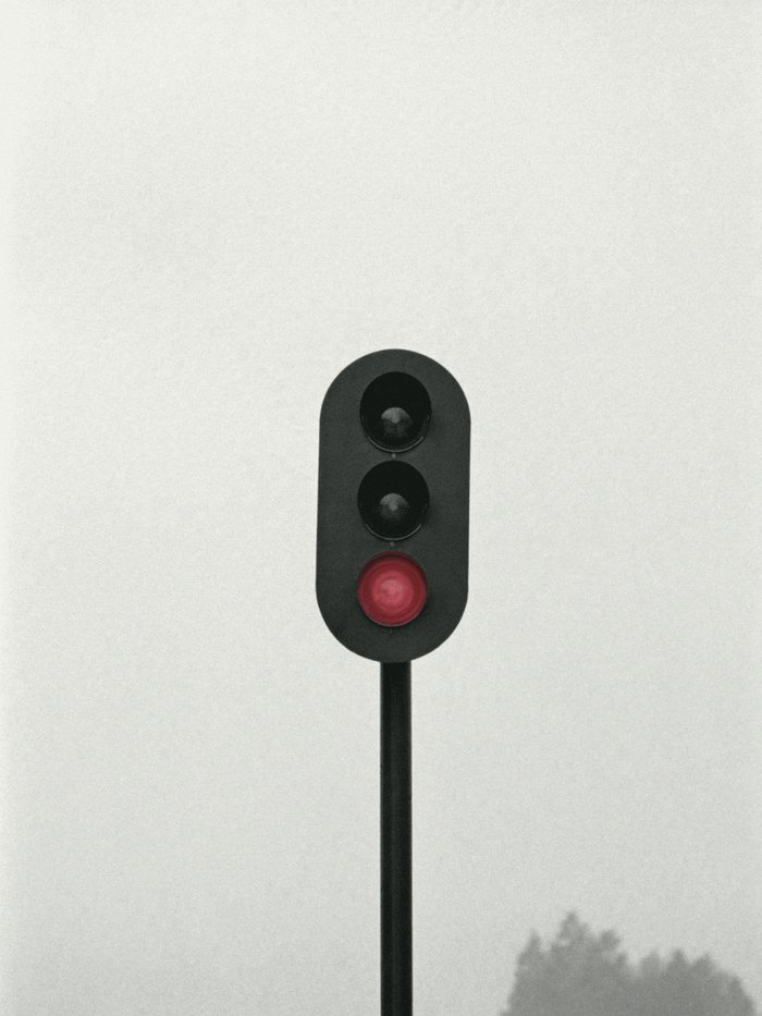 A railway signal against a pale sky, its red lamp lit.